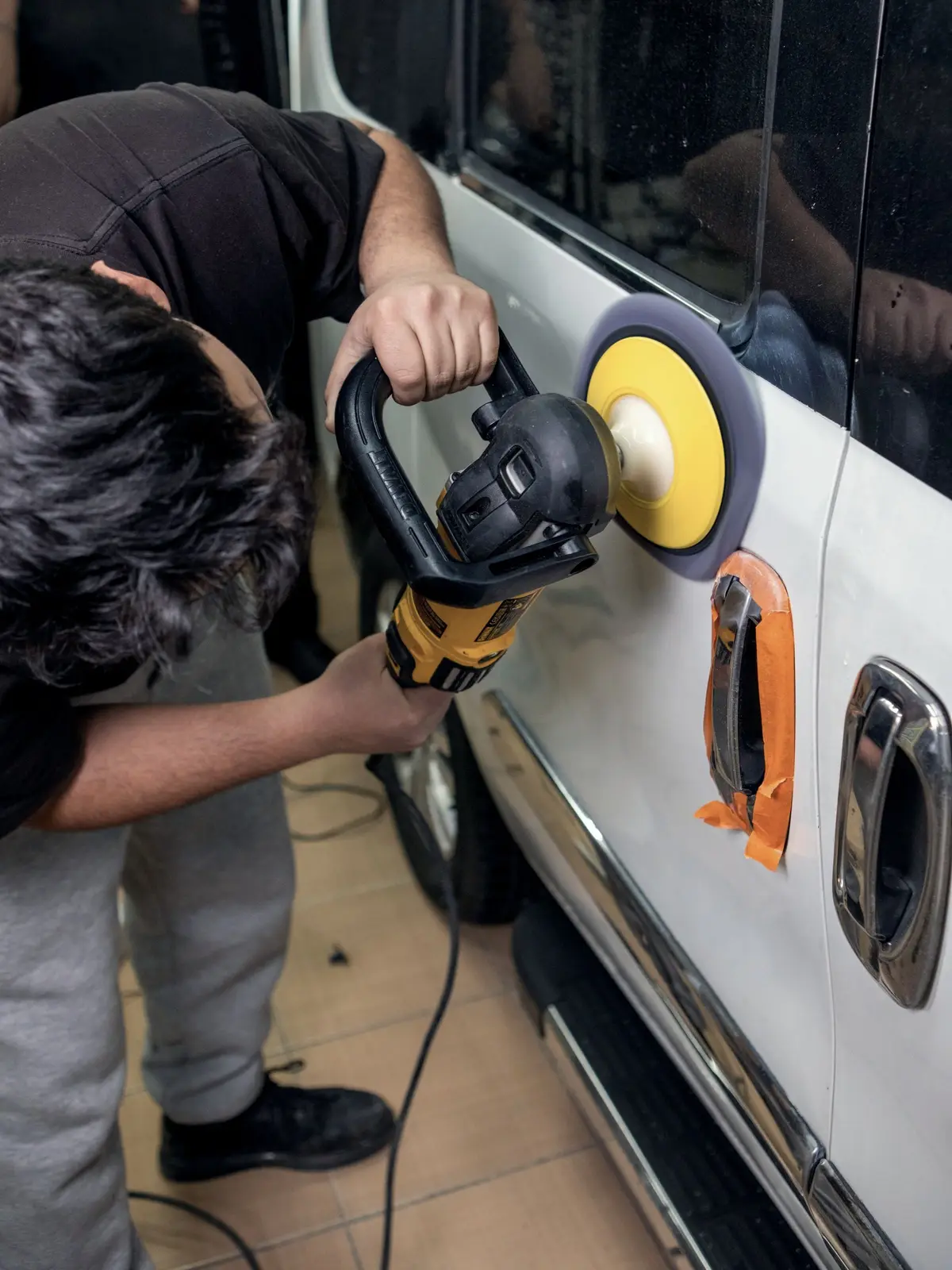 Bir teknisyen beyaz bir aracın kapısını makineyle parlatıyor